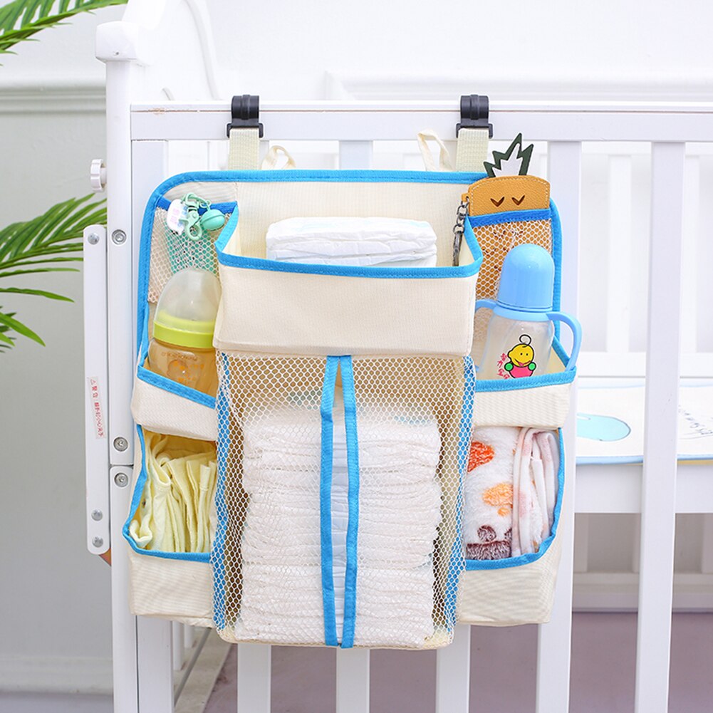 Hanging crib diaper organizer bag in cream and blue, filled with diapers and bottles on a crib rail